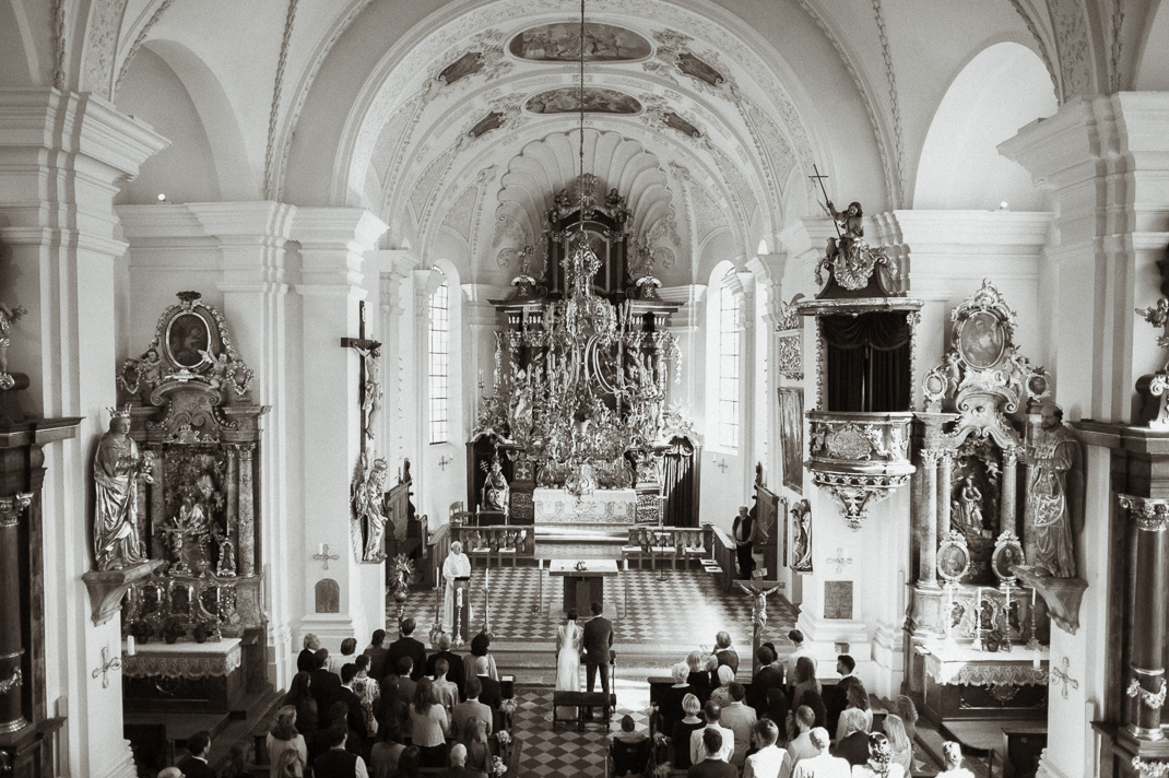 Hochzeit in der St. Sixtus Kirche am Schliersee. Übersicht von der Empore über die Hochzeitsgesellschaft in schwarzweiß. Hochzeitsfotograf Mr & Mrs Wedding.