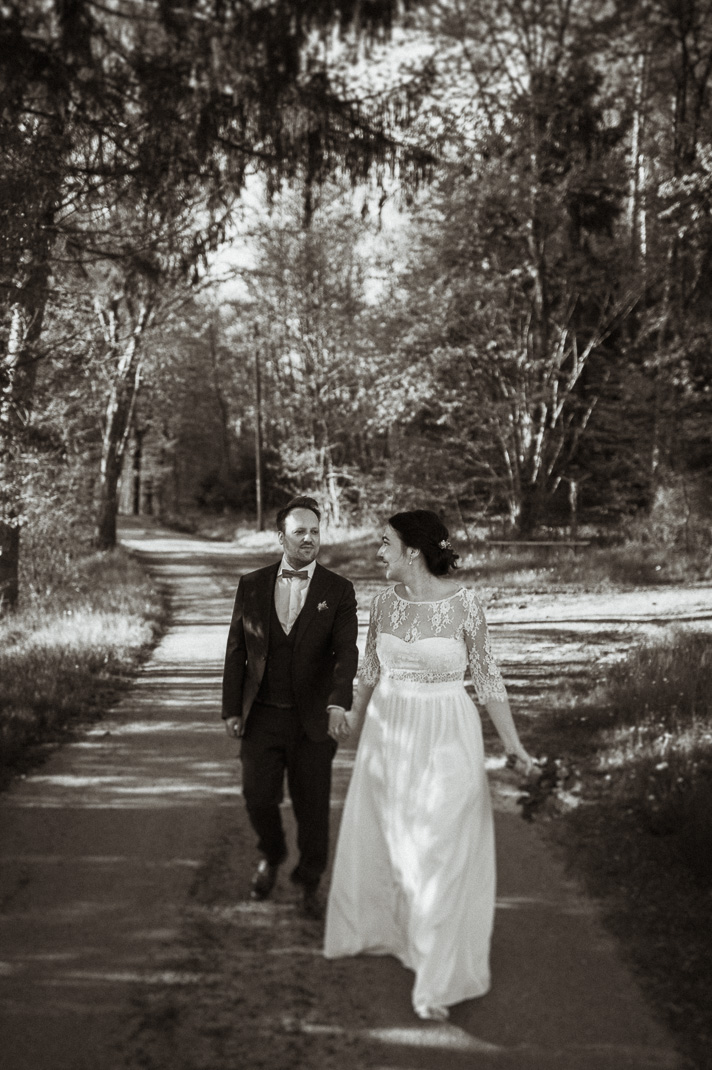 Pärchenshooting bei einer ganztages Hochzeitsbegleitung. Schwarzweißbild des Brautpaares, dass auf einem Feldweg geht. Hochzeitsfotografen sind Andreas Reiter und Manuela Reiter.