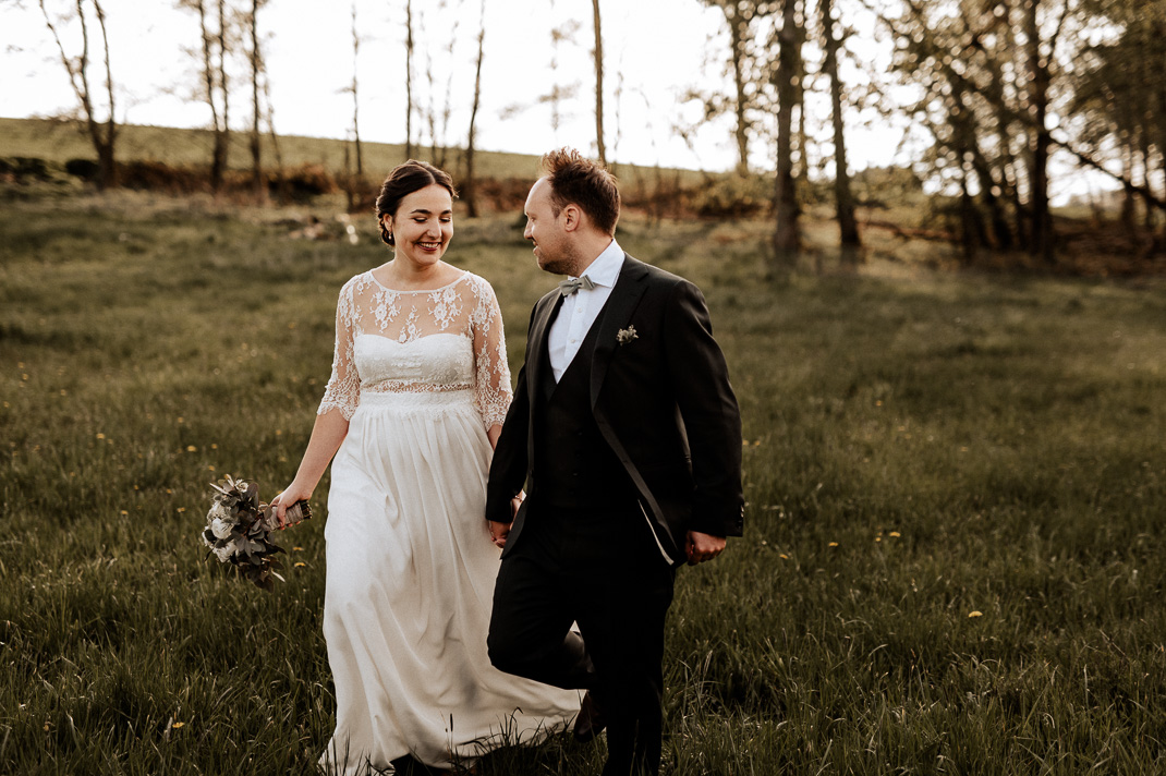 Paarfotos bei Maiers Hofstubn Hausmehring. Das Brautpaar geht lachend über eine Wiese. Hochzeitsfotograf ist Andreas Reiter.