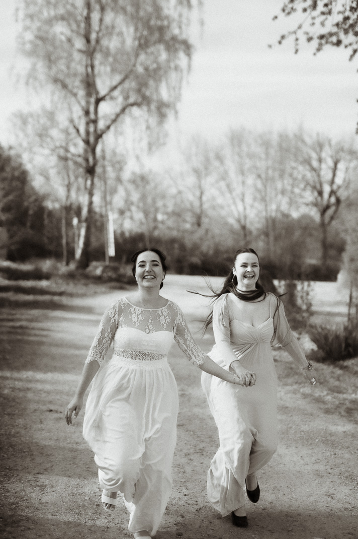 Die Braut rennt mit ihrer Trauzeugin einen Weg entlang. Lustiges Hochzeitsfoto. Hochzeitsfotografen sind Mr & Mrs Wedding aus Freising.