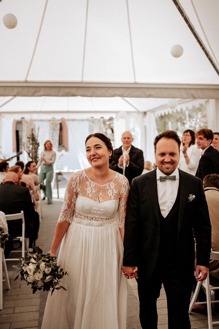 Hand in Hand verlassen Braut und Bräutigam das weiße Hochzeitszelt, umgeben von der Liebe ihrer Gäste