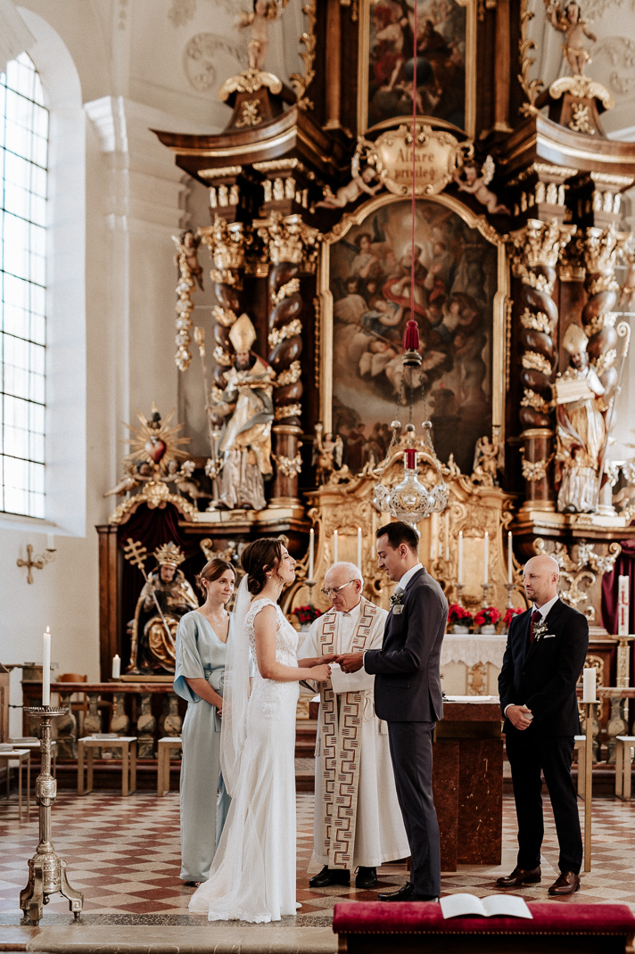 Hochzeitsfotograf Schliersee. Reportagefoto, der Bräutigam steckt seiner Braut den Ehering an.