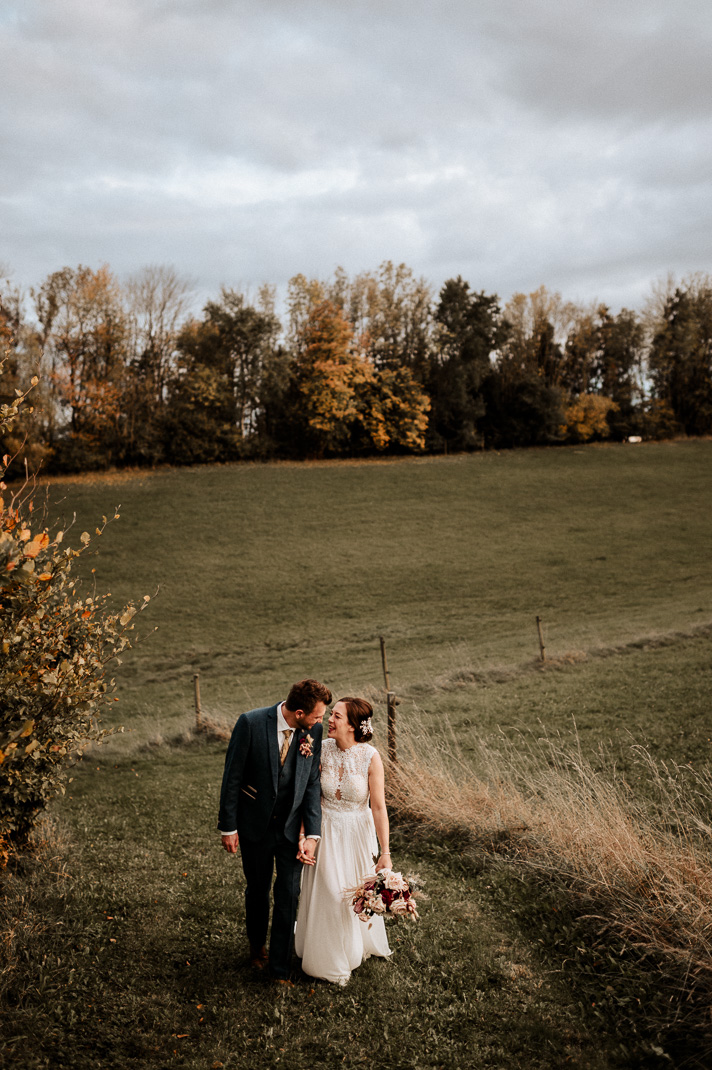 Braut und Bräutigam lachen ausgelassen, während sie durch die herbstlichen Felder von Gut Thurnsberg spazieren.