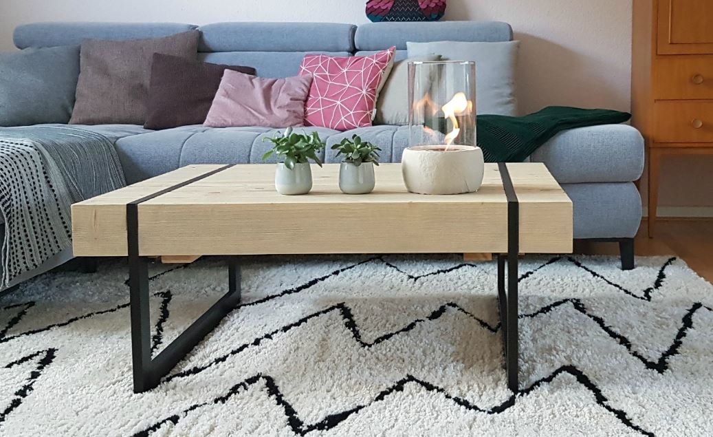 Moderner Couchtisch mit heller Holzbalken-Tischplatte und robustem Eisengestell in Kufenform.