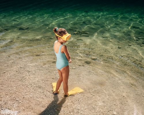 Baden mit Kindern im Salzkammergut – Kind am flachen Seeufer mit klarem Wasser und Kiesstrand