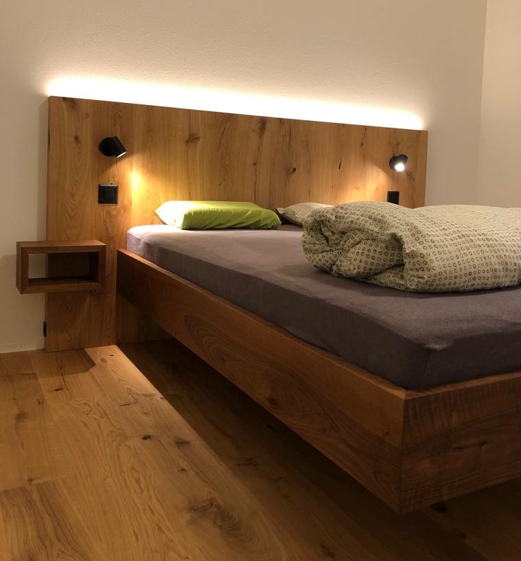 Nussbaum Bett, Kopfteil mit Parkett fliessend hochgezogen, passende Ablagen sowie integrierte Lichtquellen
