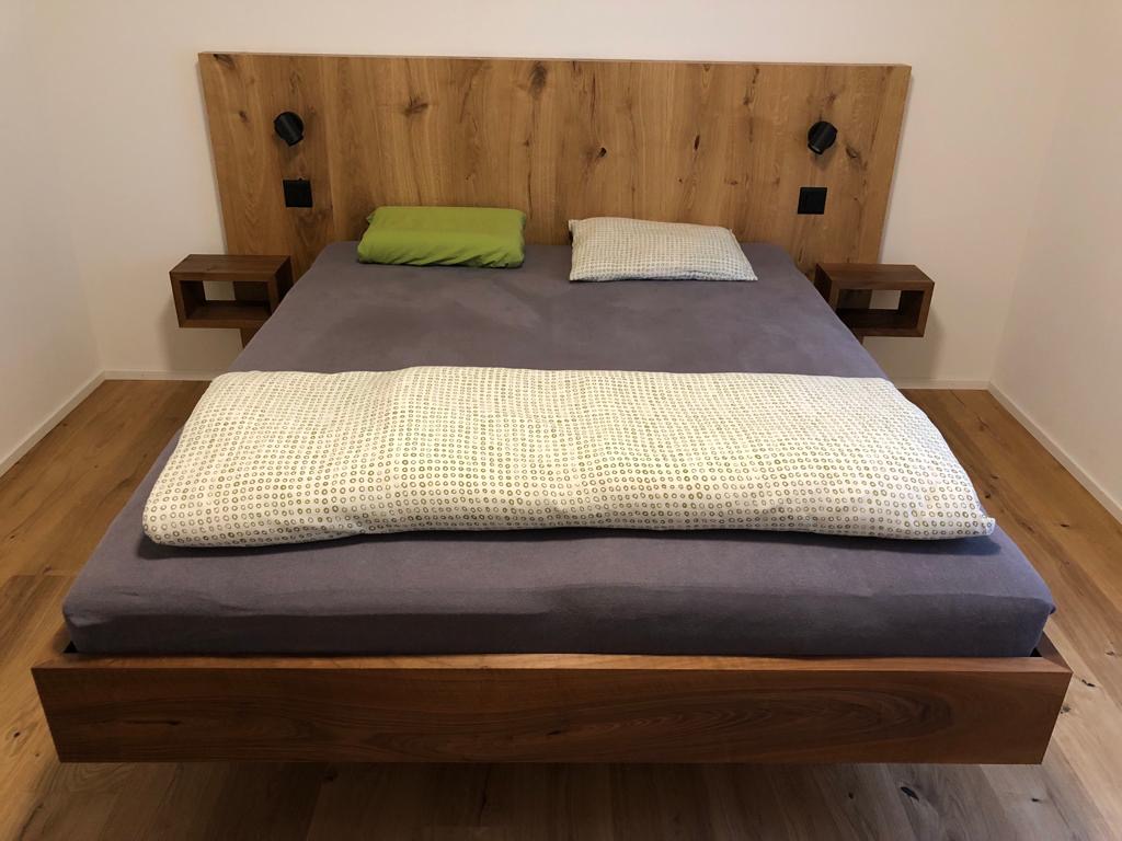 Bett Nussbaum, Kopfteil mit Parkett fliessend hochgezogen, passende Ablagen sowie integrierte Lichtquellen