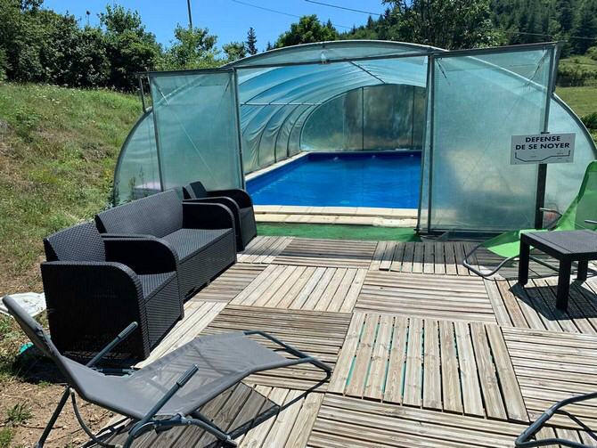 La piscine privative de couleur bleue avec un dallage blanc tout autour et sous serre du gite de la gorre en location en ardeche village de roiffieux