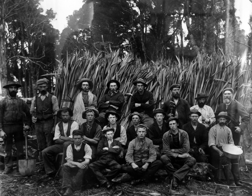 Flax mill workers in Mangakarau - flax sheaves in background and man third from left festooned in shank of processed flax (c. 1890s Tyree Studio - Photo of photo in Community Centre) 