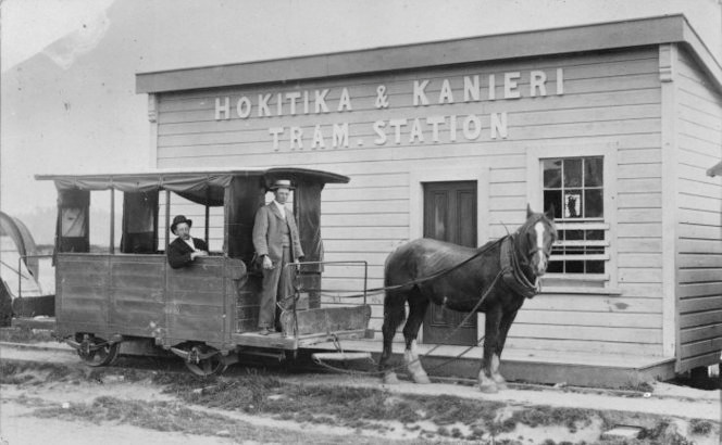 Hokitika & Kanieri tram station between 1877 and 1893. The operator Tom McGuigan sits inside and his son alongside. Ref: 1/2-018531-F. Alexander Turnbull Library, Wellington, New Zealand.