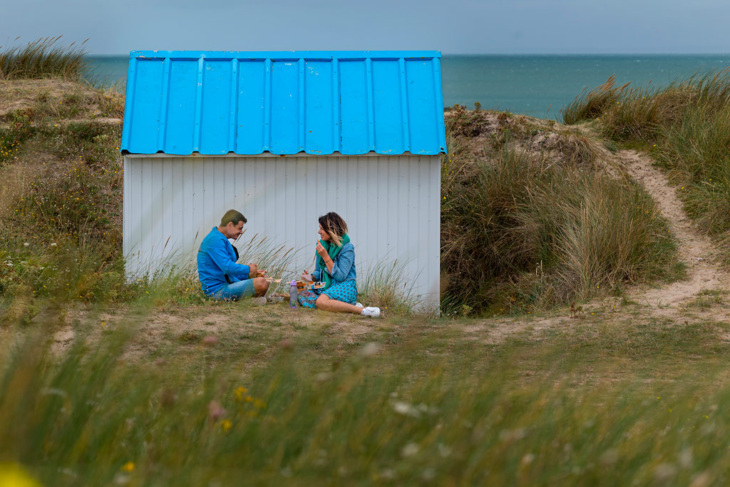 Ein Pärchen sitzt im Windschatten einer Badekabine in Gouville sur Mer.