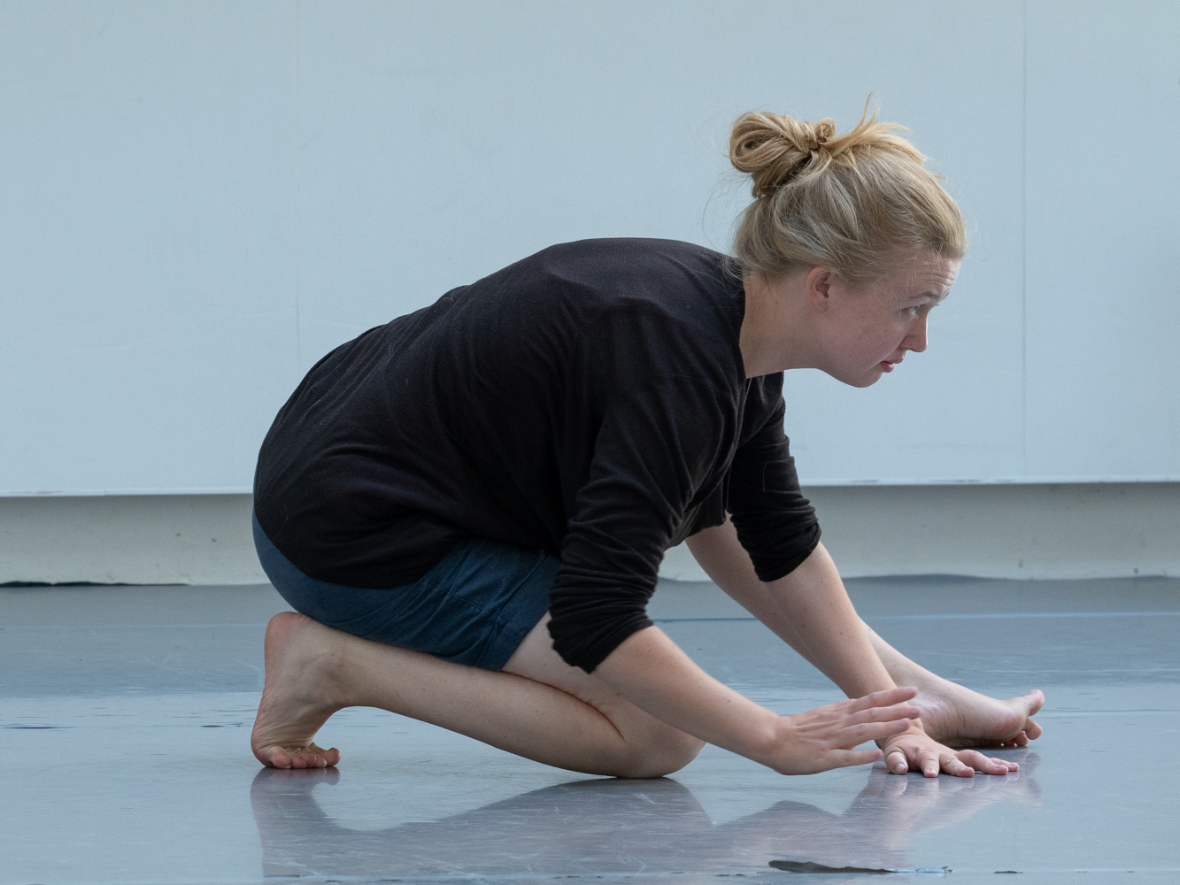 Porträt der Schauspielerin, Tänzerin und Choreografin Camilla Pölzer bei einer Theaterprobe. Sie kniet in gespannter Haltung auf dem Boden, der Blick geht konzentriert nach rechts. Sie wirkt, als könne sie jeden Moment aufspringen.