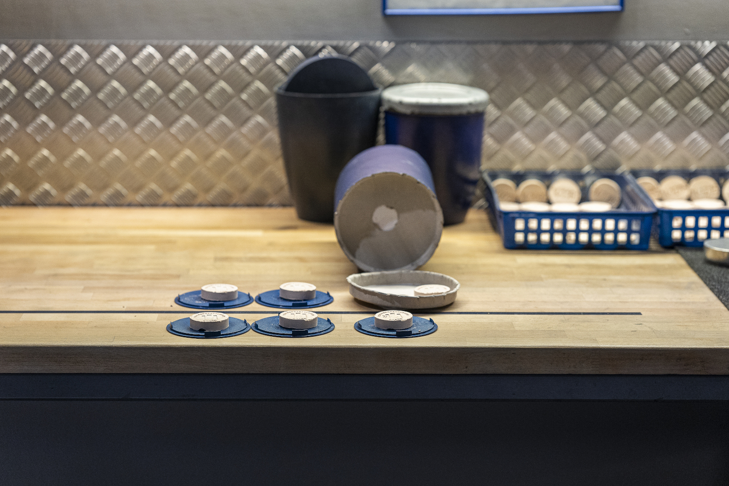 Auf einem Tisch sieht man mehrere blaue Plastik-Deckel, mit denen die Urnen im Krematorium Stade zum Schluß versiegelt werden. Auf jedem Deckel liegt ein runter Keramikstein mit der eingeprägten Identifikationsnummer für den Toten. 
