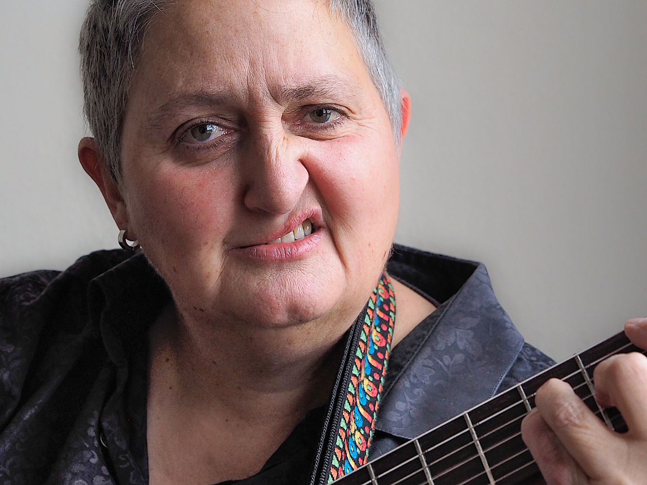Webseite-Porträt der Singer Songwriterin Jasemin Alt. Sie hat kurze graue Haare und ein eine Gitarre um den Hals. Man sieht ihre Hand auf dem Griffbrett. Sie zieht eine Schnute wir Billy Idol. 