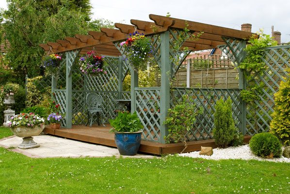 This lattice-framed garden pergola serves up a serene spot for relaxing in the shade surrounded by whimsical climbing vines and colorful hanging baskets of flowers. 