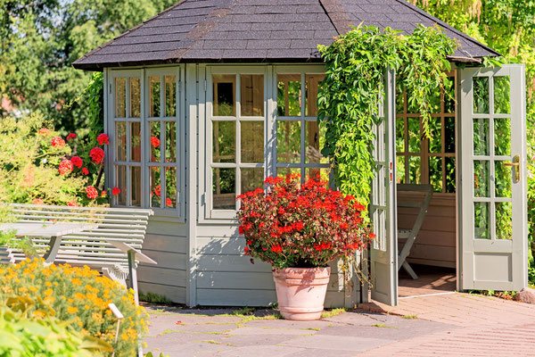 Providing outdoor seating and shelter from the sun, wind, rain and mosquitoes, this enchanting enclosed gazebo is fully framed with siding, windows, quaint French doors and a colorful variety of vegetation. 