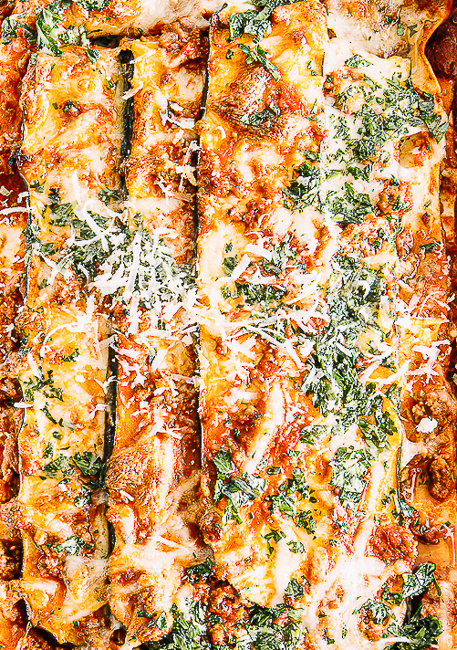 Zucchini-Lasagne mit Bolognese und goldbraunem Mozzarella in einer weißen Auflaufform, von oben fotografiert - mit gehackter Petersilie bestreut