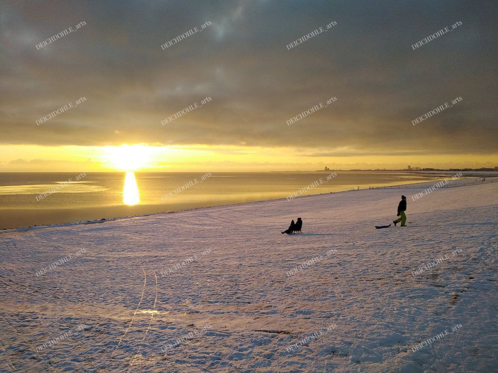 Kinder rodeln im Schnee am Deich in der Abendsonne