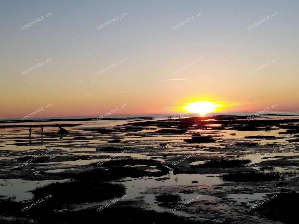 Sonne geht über dem Watt an der Nordsee unter. Im Watt spielen Kinder.