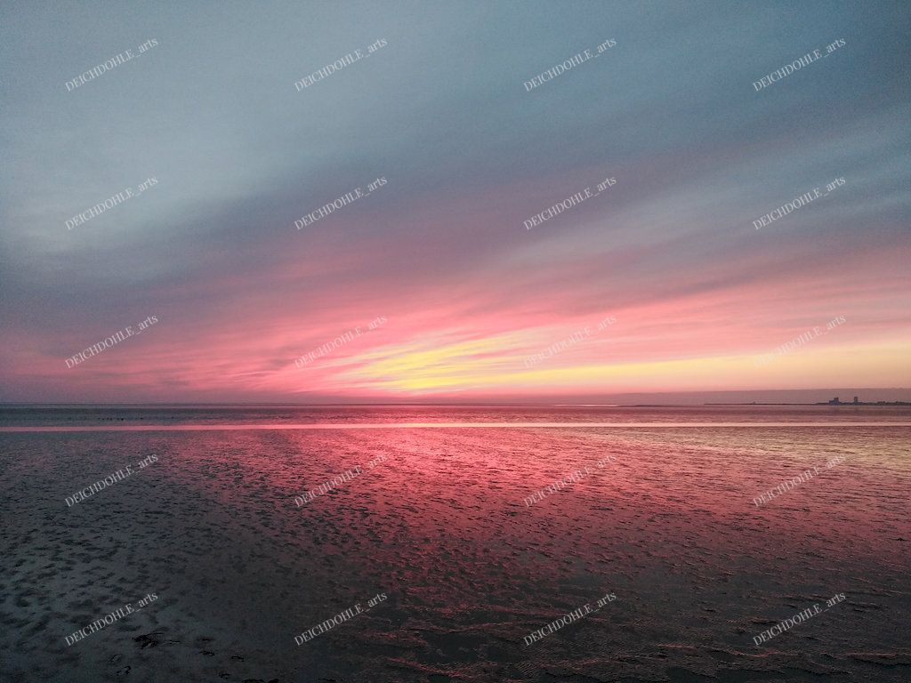 Eindrucksvoller Sonnenuntergang zwischen Wolken und Wasseroberfläche an der Meldorfer Bucht