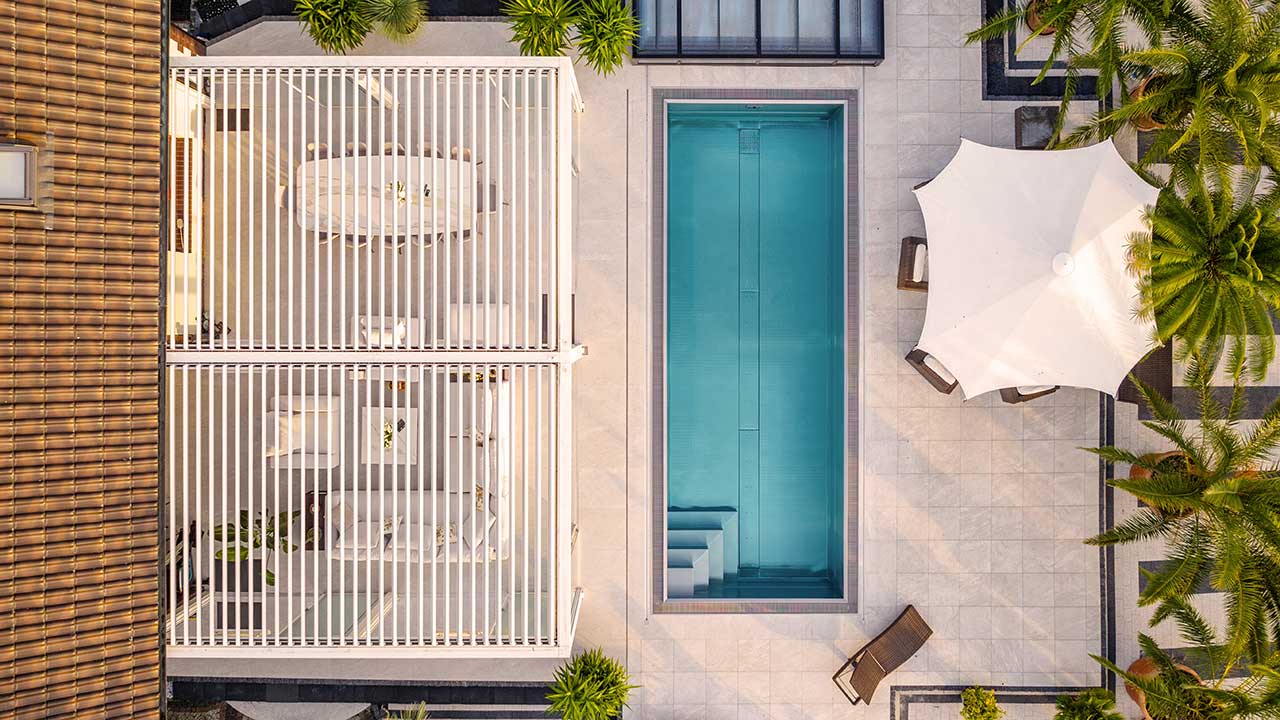 Drohnenaufnahme einer Terrasse mit Lamellendach Pergola direkt neben einem rießigen Pool
