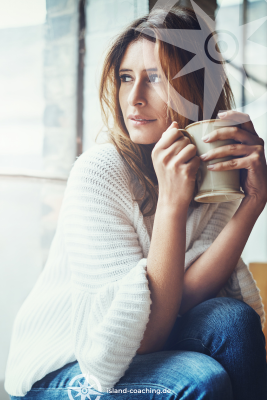 Eine Frau sitzt erschöpft mit einer Tasse Tee am Fenster: Innere Leere & Erschöpfung erlebt, wer regelmäßig seine Bedürfnisse übergeht.