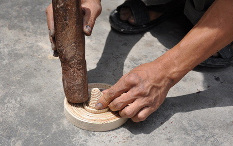   L'artisan finit sa galette de base en rentrant en force une pièce conique en lamelles de bambou, afin de maintenir et solidifier toute la structure.