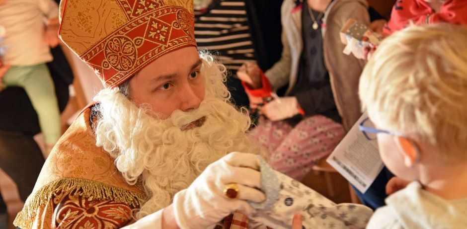 Bischof Nikolaus überreicht kniend einem kleinen Jungen ein Geschenk.