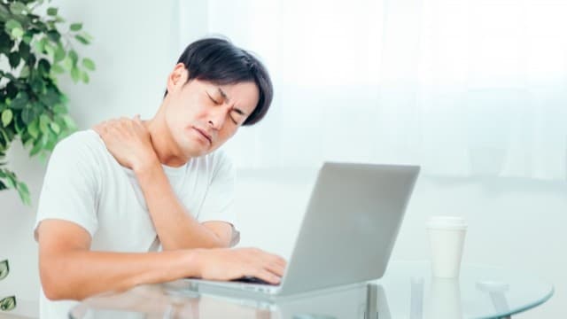デスクワークで肩こりに悩む男性