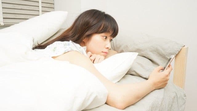 寝る前にスマートフォンを見る女性の写真