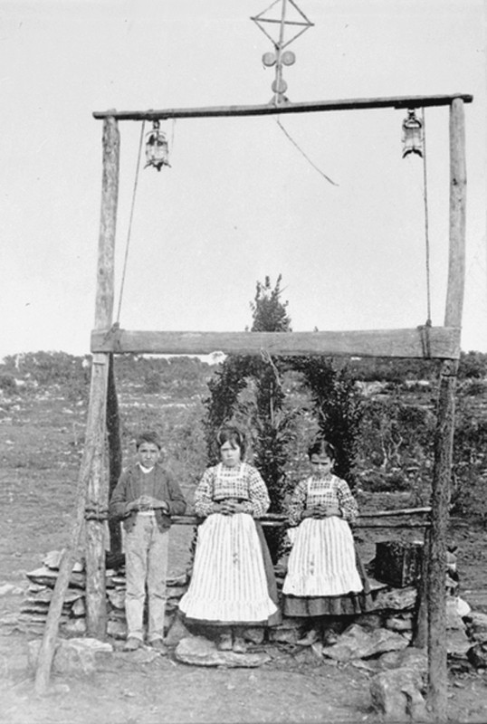 I tre "pastorinhos" Lúcia dos Santos (al centro) coi cugini Francisco e Jacinta Marto, sotto lo steccato innalzato dalla famiglia Carreira - detto "l'arco" -, per marcare il luogo delle Apparizioni  (fotografia posteriore al 13 ottobre 1917)