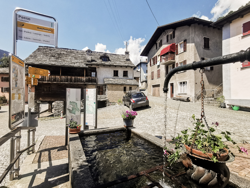 A typical village scene. Fountain with flowers, a bus stop cobblestone roads