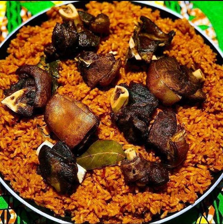 Smoky Jollof Rice with Tender Meat A hearty platter of richly seasoned jollof rice topped with succulent slow-cooked meat and aromatic bay leaves, bursting with bold flavors and traditional West African comfort.