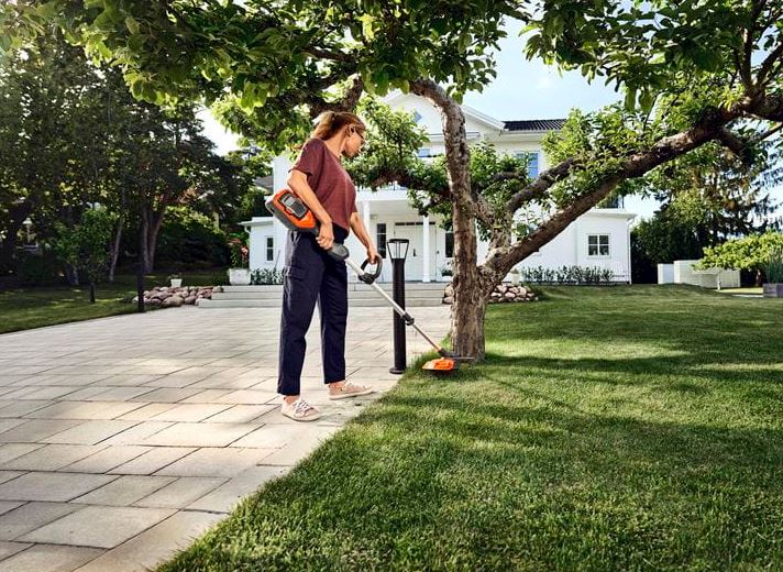 Frau am Rasentrimmen am Baum mit Akku Sense 215iL