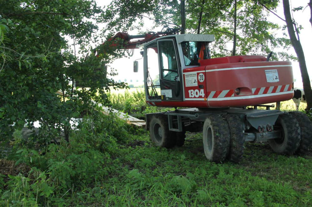 Am 24.7.12 sind endlich sind die ersten Genehmigungen da. Sofort wird mit dem Dammbau begonnen um die Baustelle trocken zulegen. Hier setzt der Bagger die Balkensperre, in Flussrichtung betrachtet, hinter das Streichwehr.