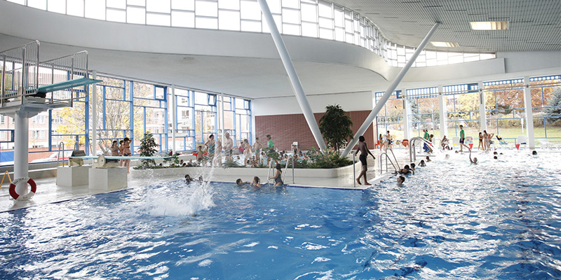 Hallenbad von Innen mit vielen Besuchern und einem Sprungturm