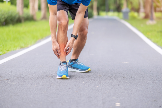 Läufer mit Schienbeinkantensyndrom und Schmerzen in den Unterschenkeln beugt sich nach vorne und berührt schmerzenden Unterschenkel
