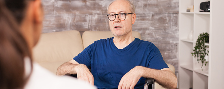 Ein älterer Herr im Rollstuhl befindet sich mit einer Fachkraft im Gespräch 