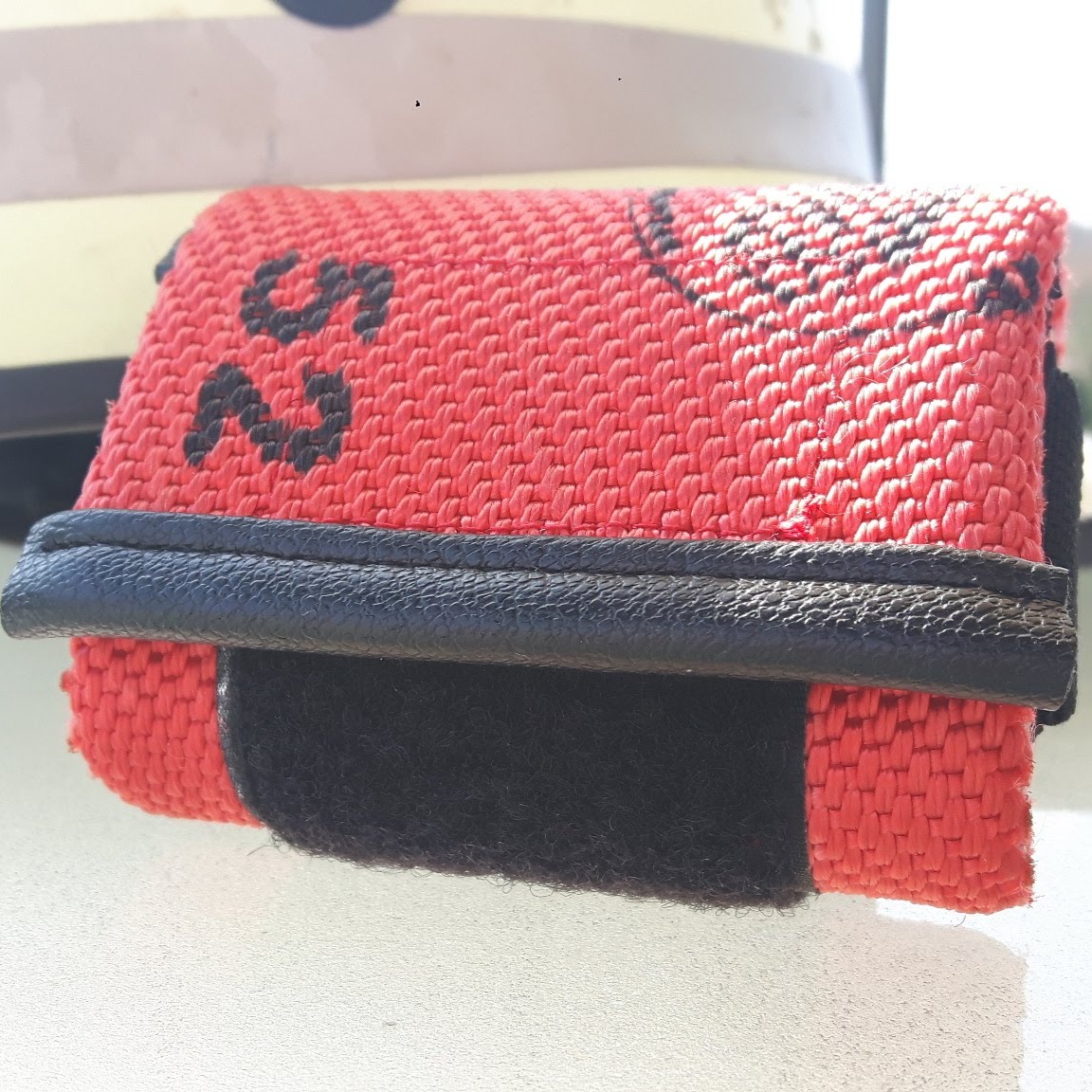 Nahaufnahme eines roten Upcycling-Produkts aus altem Feuerwehrschlauch mit schwarzem Klettverschluss, Lederkante und aufgedruckter Nummer 52.