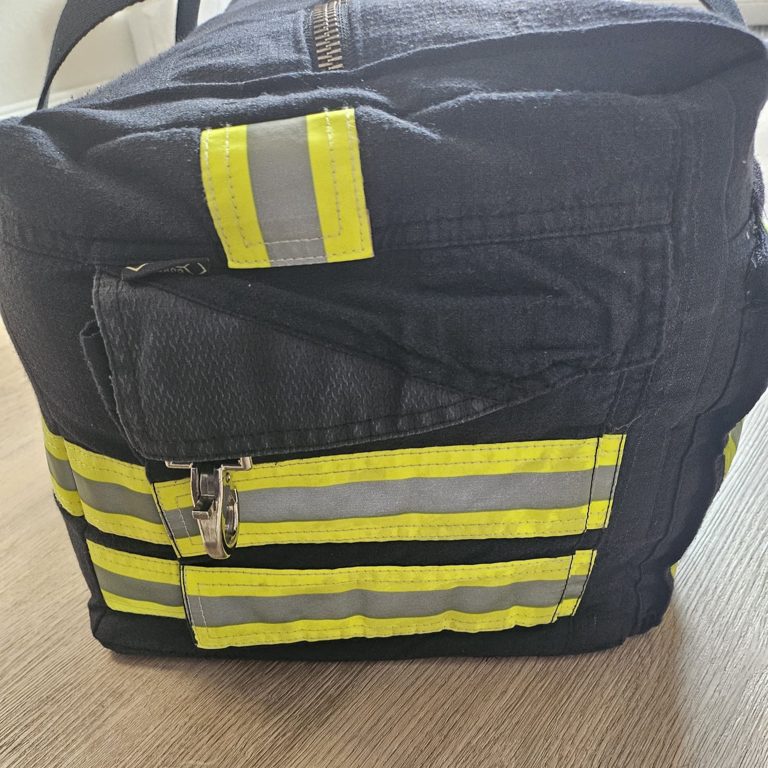 Geschlossene Stirnseite einer dunkelblauen Feuerwehr-Tasche mit Karabinerverschluss und breiten Reflexstreifen