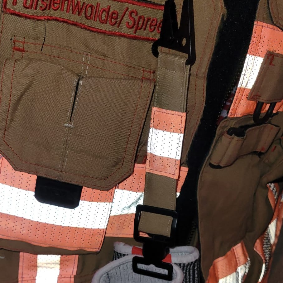 Nahaufnahme einer beigen Feuerwehrjacke aus Fürstenwalde mit reflektierenden Streifen und Ausrüstungsschlaufen vor dem Upcycling zu Taschen.