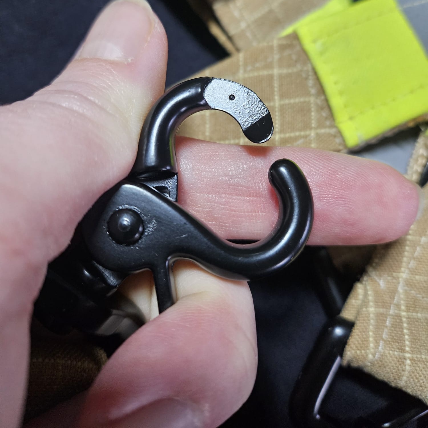 Nahaufnahme eines geöffneten schwarzen HK-Karabiners aus Metall, befestigt an einer robusten Stoffschlaufe aus beigem Feuerwehr-Upcycling-Material.