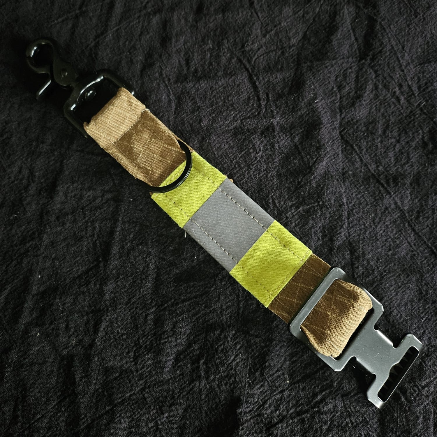 Handschuhhalter aus beigem Feuerwehr-Einsatzstoff mit gelb-silbernem Reflexstreifen, schwarzem Karabiner und Metallschnalle auf dunklem Tuch