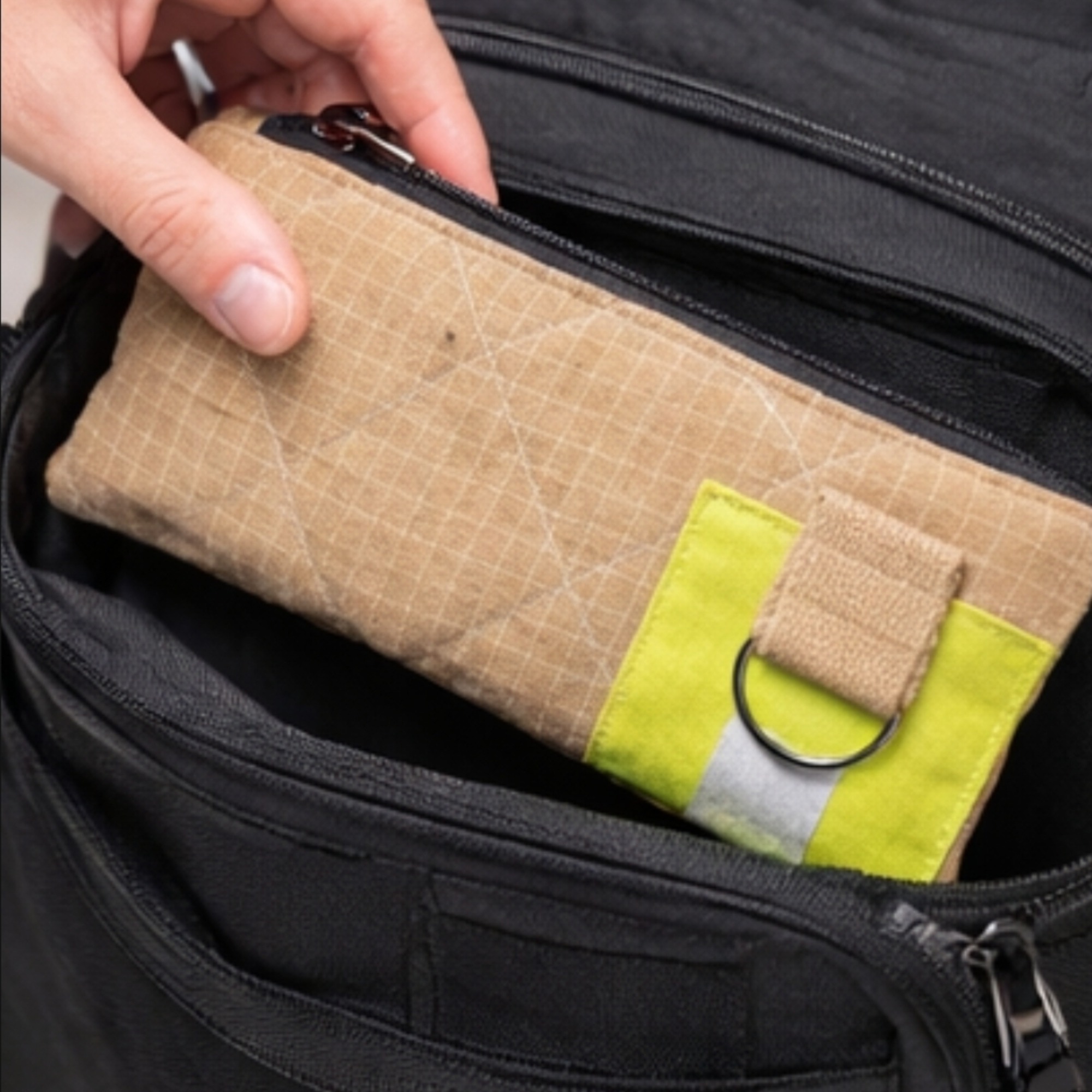 Handliches UNIT 112 Upcycling-Etui beim Einpacken in einen schwarzen Rucksack als praktischer Reise-Organizer.
