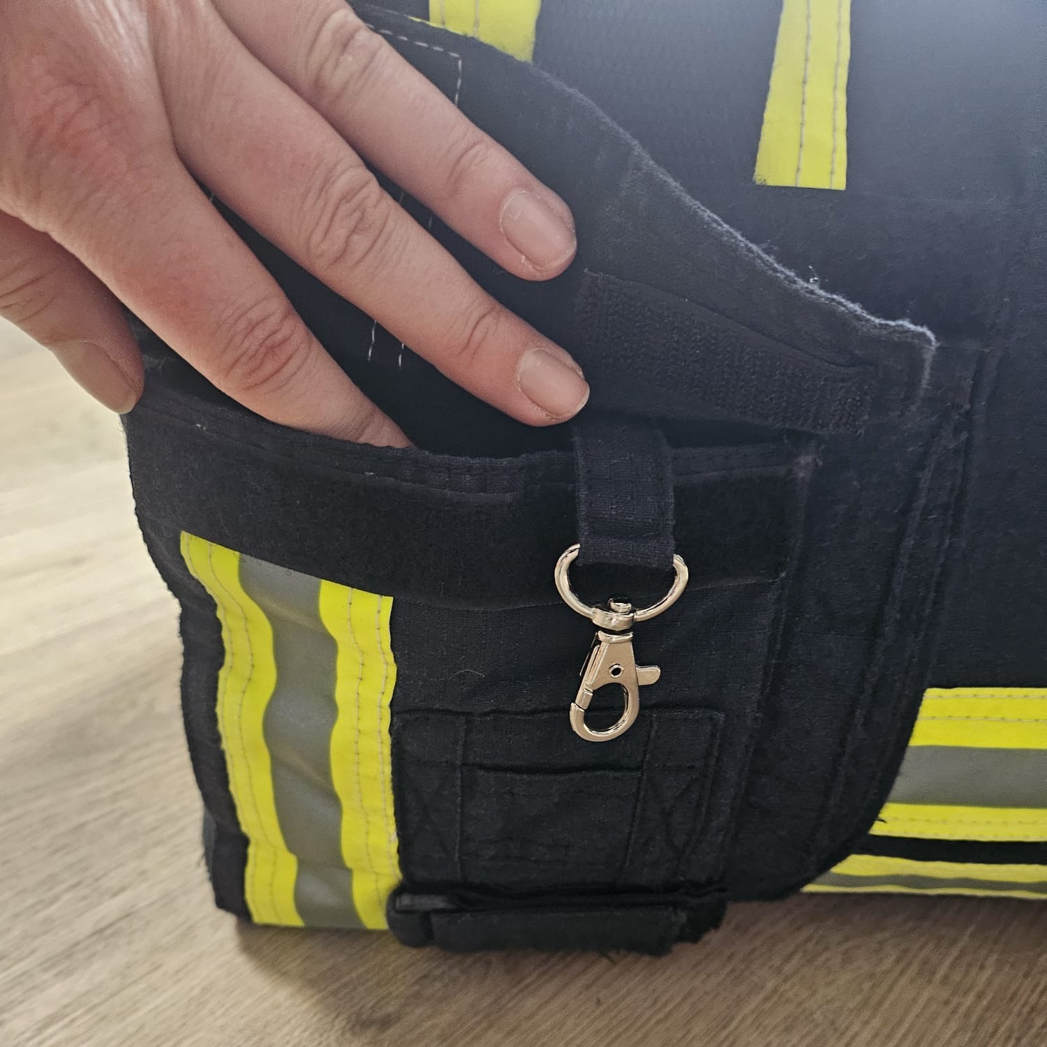 Geöffnetes Außenfach einer dunkelblauen Feuerwehr-Tasche mit Karabinerhaken und Klettverschluss
