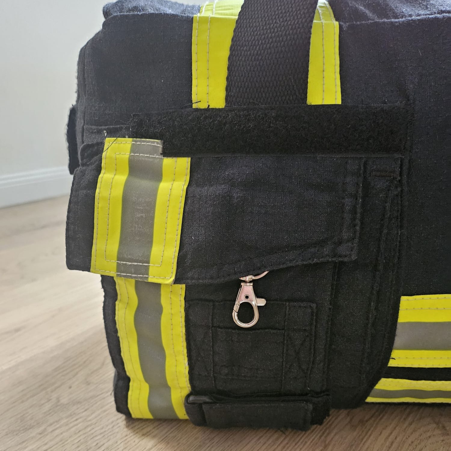 Geschlossene Außentasche einer dunkelblauen Feuerwehr-Tasche mit Karabiner, Klettstreifen und gelben Reflexstreifen