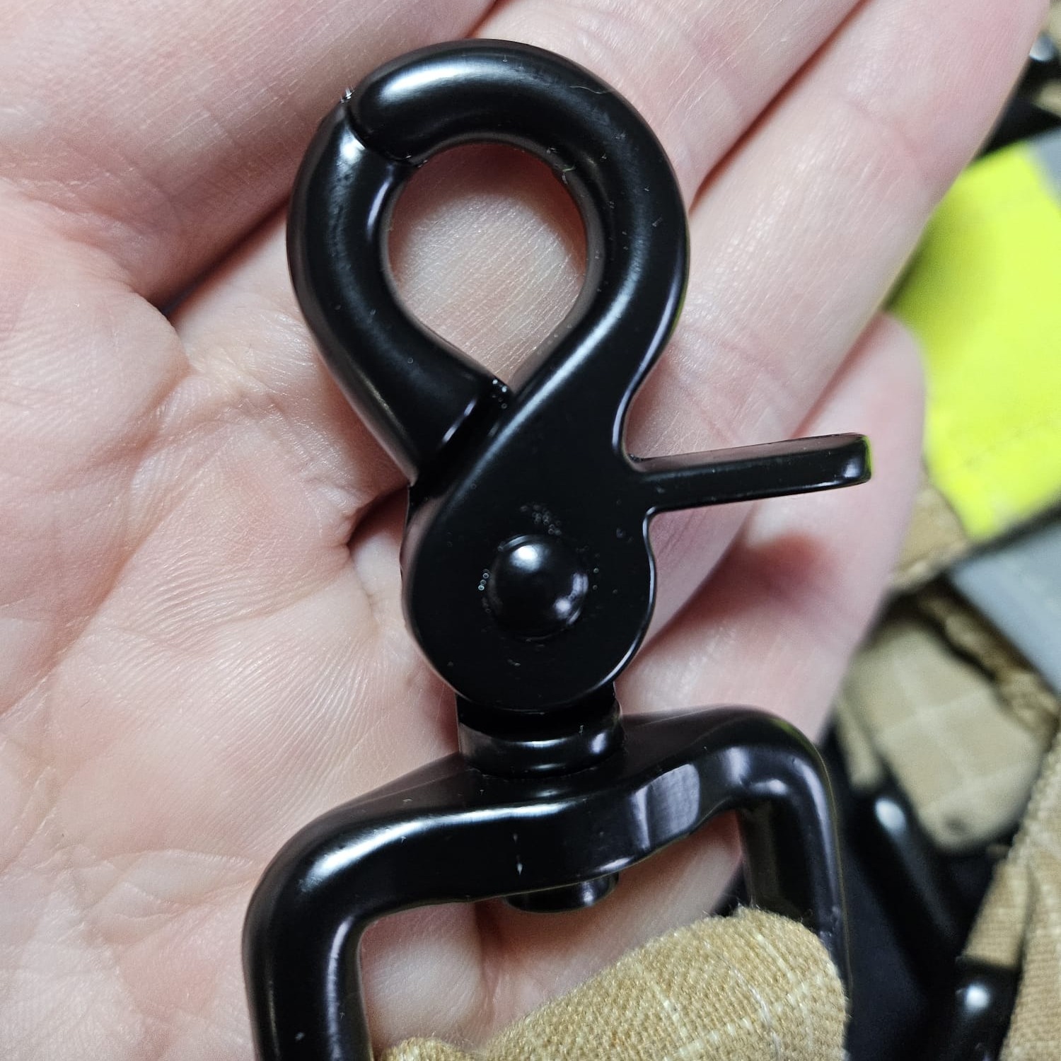 Nahaufnahme eines schwarzen Karabiners aus Metall, befestigt an einer robusten Stoffschlaufe aus beigem Feuerwehr-Upcycling-Material.