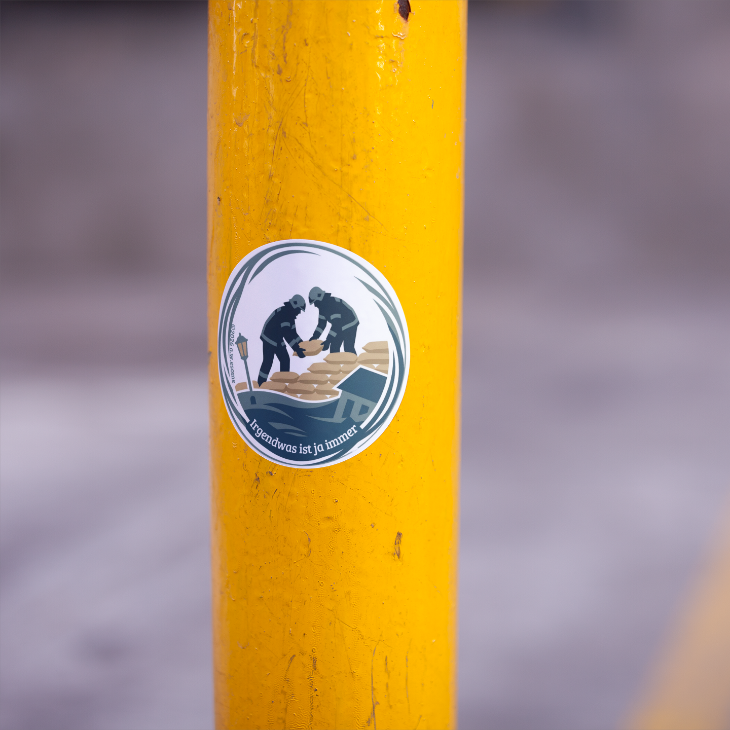 Runder Feuerwehr-Sticker mit Hochwasser-Motiv, aufgeklebt auf einem gelben Metallpfosten im Außenbereich als Anwendungsbeispiel.