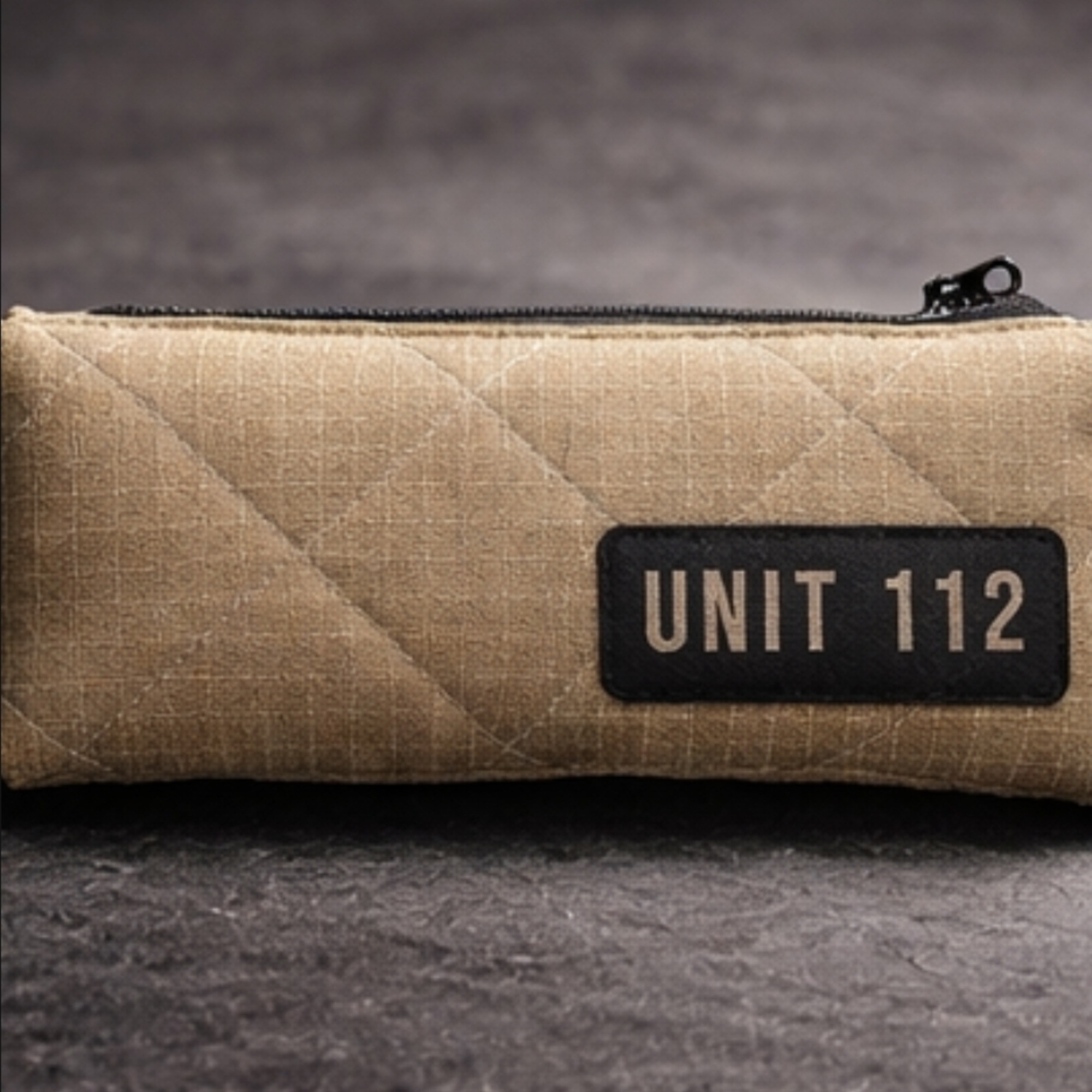 Nahaufnahme der gesteppten Feuerwehr-Federtasche mit schwarzem UNIT 112 Aufdruck auf beigem Aramid-Stoff.