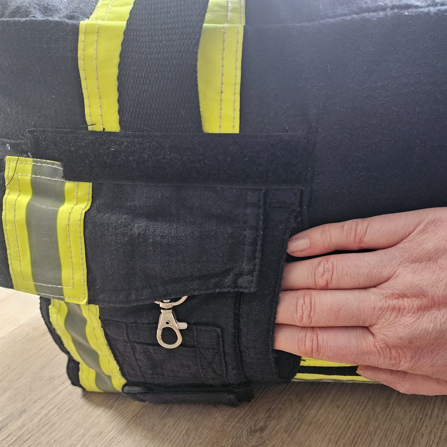Eine Hand greift in das seitliche Außenfach einer dunkelblauen Feuerwehr-Tasche mit Reflexstreifen